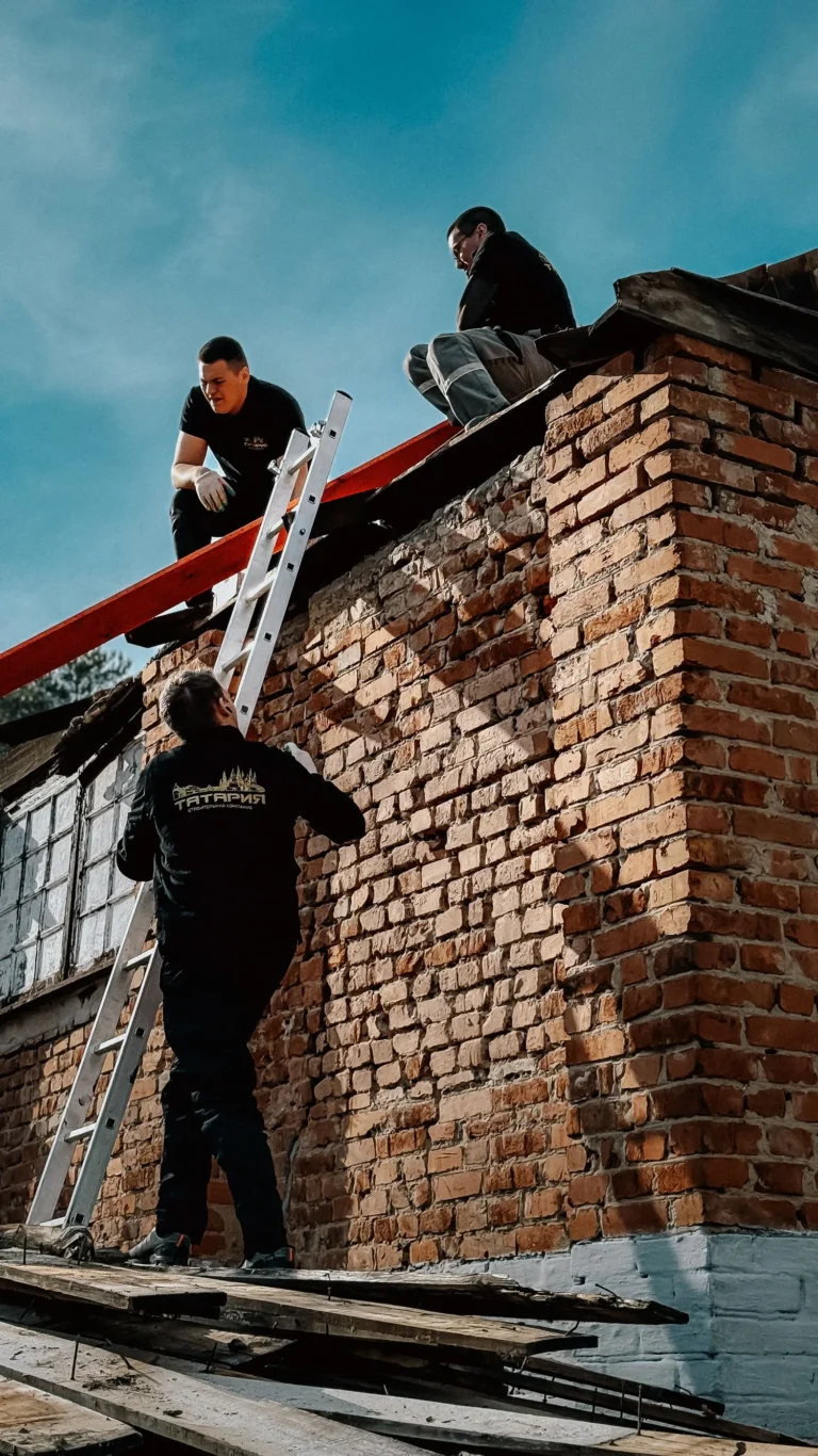 Zwei Dachdecker arbeiten mit Leiter an der Traufe eines Backsteingiebels