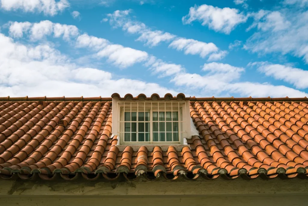 Saniertes rotes Ziegeldach mit Gaubenfenster vor blauem Himmel
